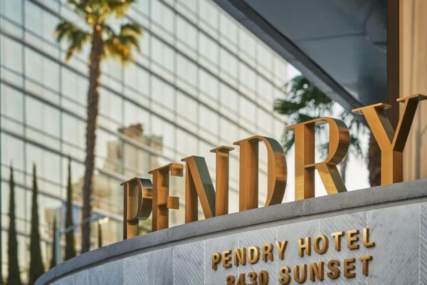 The image shows the entrance signage for Pendry West Hollywood at 8430 Sunset. The golden letters "PENDRY" are prominently displayed against a backdrop of a tall reflective building and palm trees, giving a luxurious and sunny atmosphere reminiscent of nearby Universal Studios.