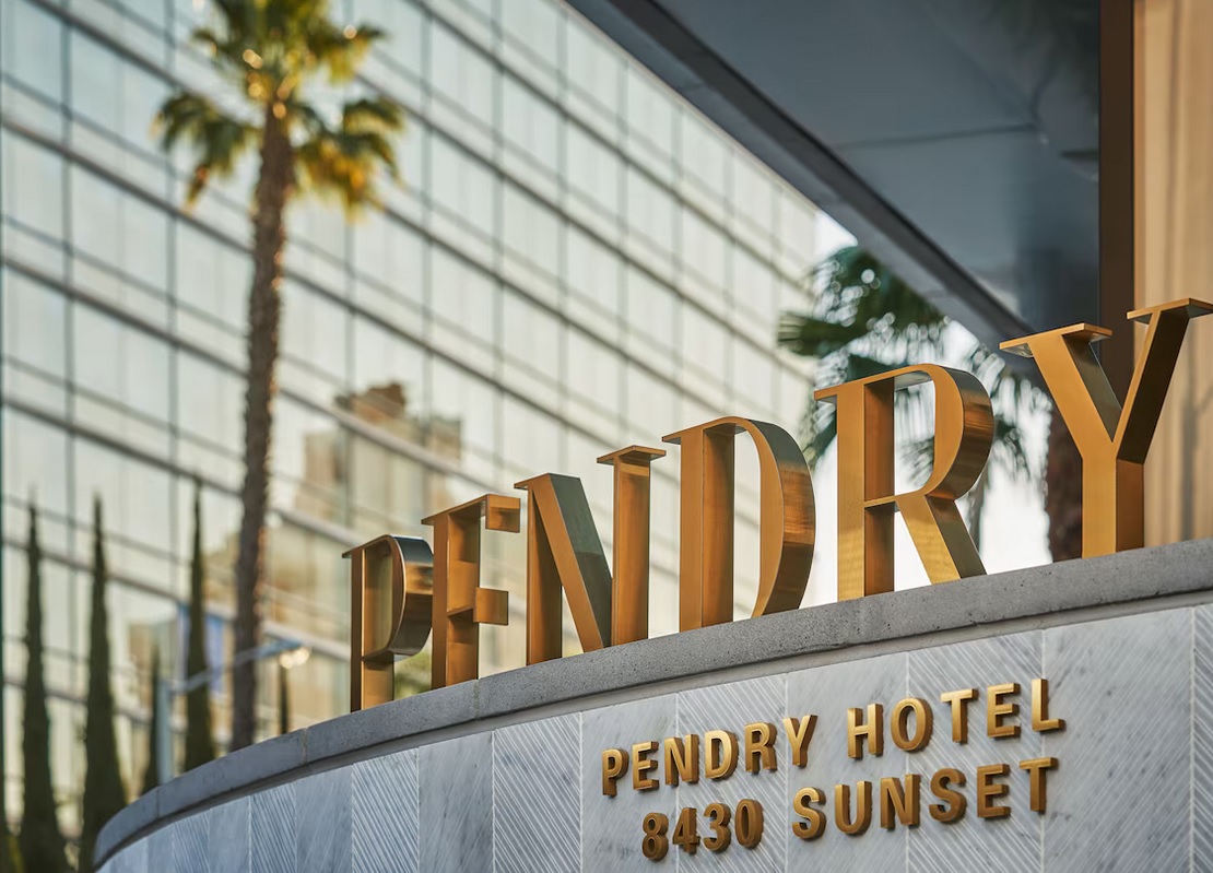 The image shows the entrance signage for Pendry West Hollywood at 8430 Sunset. The golden letters "PENDRY" are prominently displayed against a backdrop of a tall reflective building and palm trees, giving a luxurious and sunny atmosphere reminiscent of nearby Universal Studios.